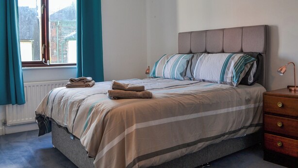 Een slaapkamer met een bed, een raam met gordijnen, een radiator en een nachtkastje met een lamp.