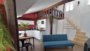 Een modern interieur met een houten trap, een blauwe bank, een eethoek met een tafel en stoelen, en een keuken op de achtergrond.