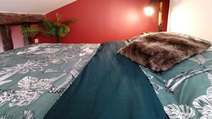 Een slaapkamer met een bed, een rode muur, een plant en een lamp.