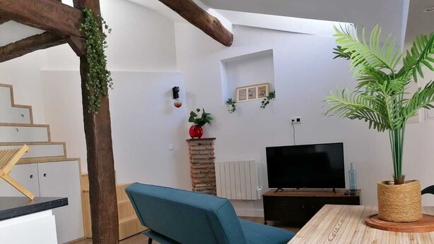 Een moderne woonkamer met een blauwe bank, een houten tafel, een televisie en een trap met een houten balk.