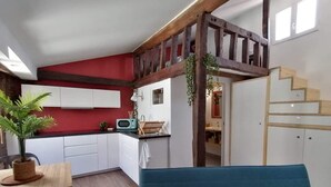 Een ruimtelijk ingerichte leefruimte met kitchenette, een eethoek en een trap naar een hoger niveau.