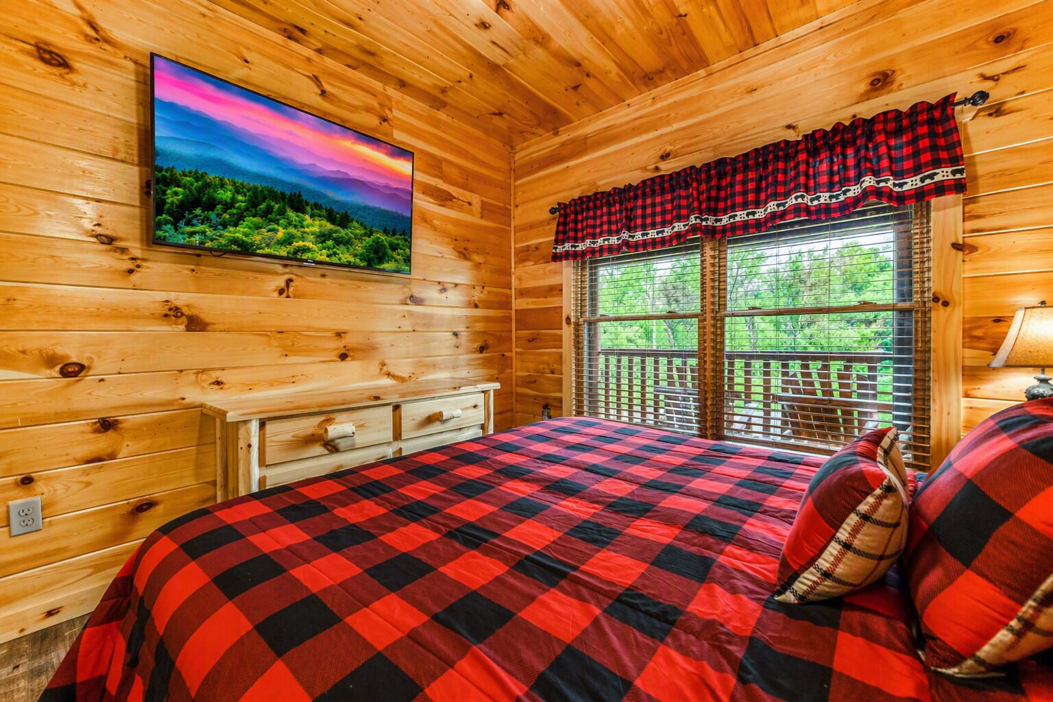 Une pièce de style cabane en bois, avec un lit, un téléviseur fixé au mur et une fenêtre donnant sur un paysage verdoyant.