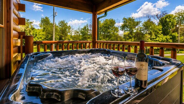 Ein Whirlpool mit zwei Weingläsern, einer Flasche und einer Holzterrasse mit Geländer.