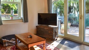 Een gezellige woonkamer met een televisie op een houten kast, een klein tafeltje met een afstandsbediening, een raam met gordijnen, en een schuifdeur van glas die leidt naar een buitenruimte.