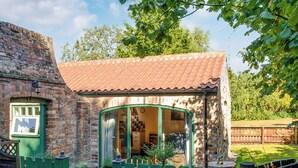 Een klein, bakstenen huis met een pannendak, een groene deur en een raam met gordijnen.
