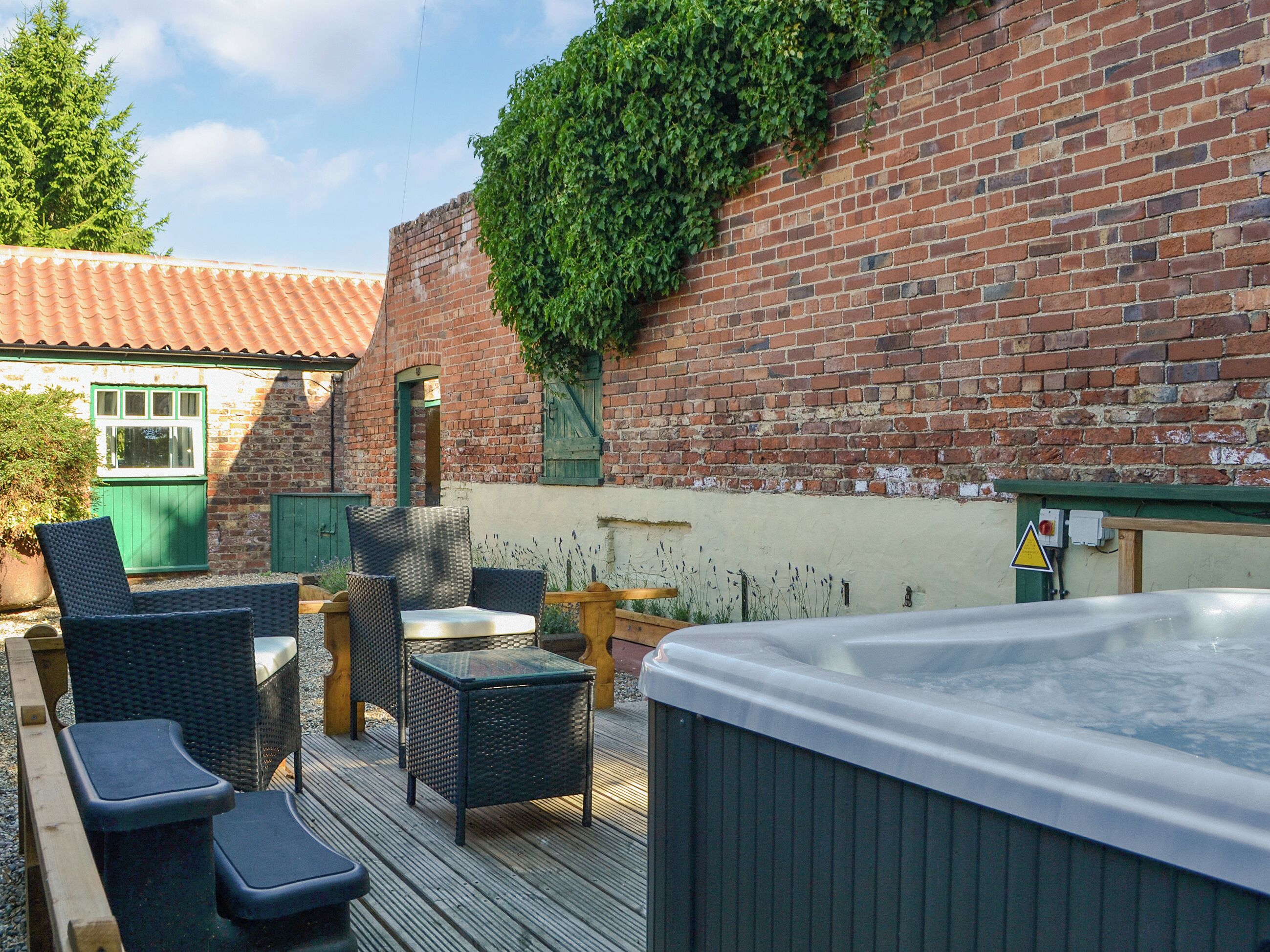 Une terrasse extérieure avec des meubles en osier, un jacuzzi et un mur de briques orné de plantes grimpantes.