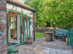 Una casa de ladrillo con una puerta verde, un banco de madera y una pequeña mesa con una estatua.