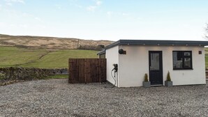Un petit bâtiment d’un seul étage, avec une allée gravillonnée, une clôture en bois et un mur de pierres.