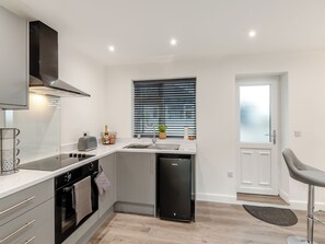 A modern kitchen with a built-in oven, a dishwasher, and a window with blinds.