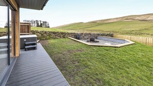 Une terrasse extérieure moderne, agrémentée d’un mur en pierre, d’un foyer et d’un espace paysager verdoyant.