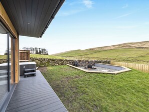 A modern outdoor deck with a stone wall, a fire pit, and a grassy landscape.