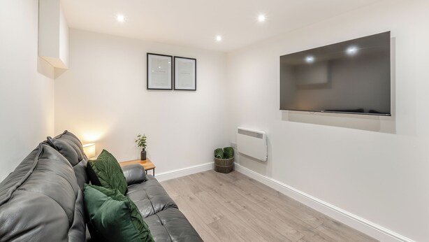 Un salon moderne avec un canapé gris, un téléviseur à écran plat, des certificats encadrés accrochés au mur et une petite table sur laquelle est posée une plante.
