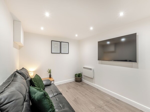 A modern living room with a grey sofa, a flat-screen TV, framed certificates on the wall, and a small table with a plant.