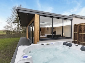 Een modern huis met een jacuzzi, grote schuifpuien en een overdekt terras.