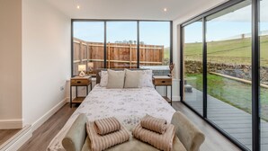 Une chambre avec un grand lit, une lucarne, une vue sur la campagne et une clôture en bois.