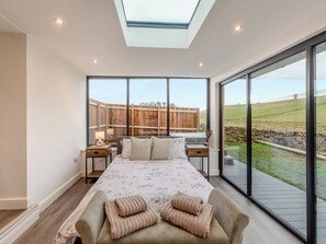A bedroom with a large bed, a skylight, a view of the countryside, and a wooden fence.