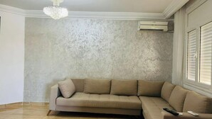 Una sala de estar con un sofá seccional color beige, una araña y piso de baldosas.