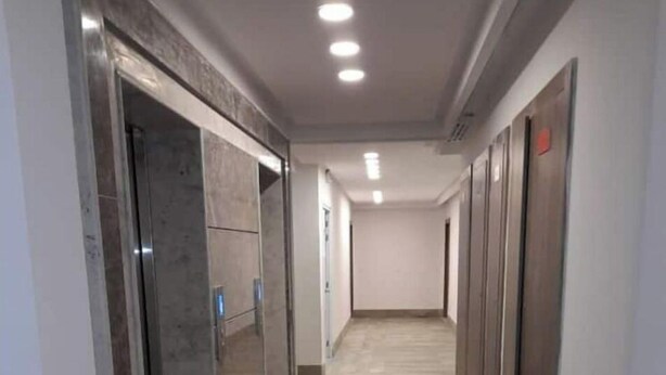 Un pasillo con suelo de baldosas, puerta de ascensor de vidrio y una pared lisa con una puerta al final.