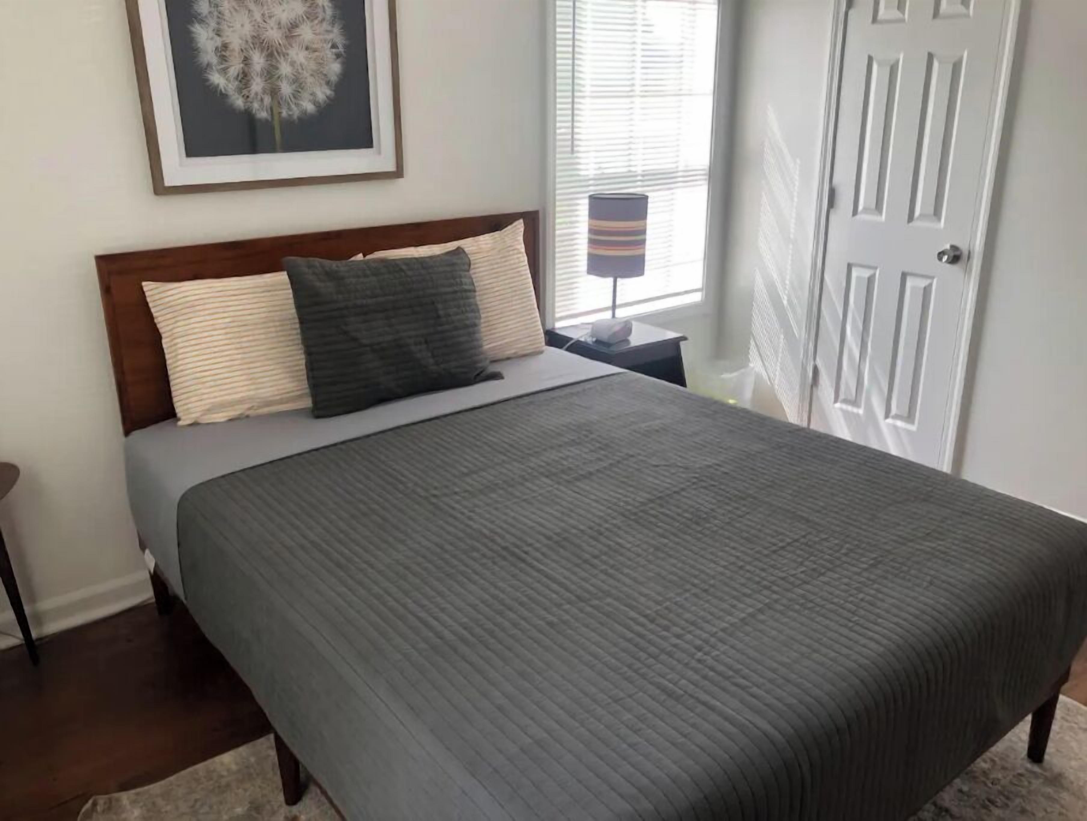 A neatly made bed with a grey quilt, a wooden headboard, and two pillows.