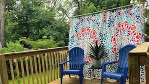 A wooden deck with two blue chairs and a table, surrounded by a colorful floral-patterned backdrop. - “Mint City w Soul...” 2BR 5 min to Stadium & UMMC! (Jackson)