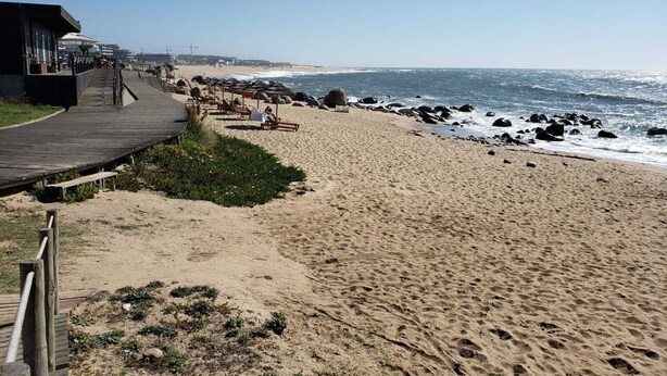 Une plage avec une promenade en bois menant à un bâtiment doté d’une façade en verre.