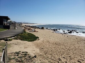 Ein Strand mit einer Holzpromenade, die zu einem Gebäude mit Glasfassade führt.