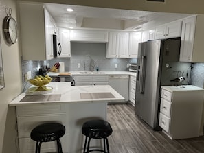 A modern kitchen with white cabinetry, a stainless steel refrigerator, a built-in dishwasher, and a central island with stools.