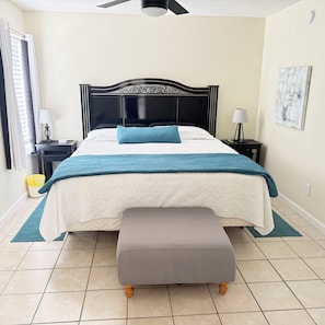 A bedroom with a bed, bedside tables, a bench, a ceiling fan, and a wall-mounted artwork.