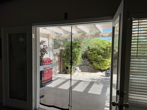 A sliding glass door leading to a patio area with a barbecue grill, a stone wall, and a small tree.