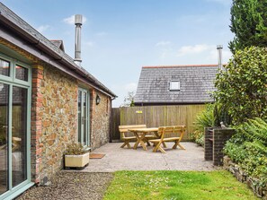 A stone building with a wooden deck, a table and chairs, and a small garden area.
