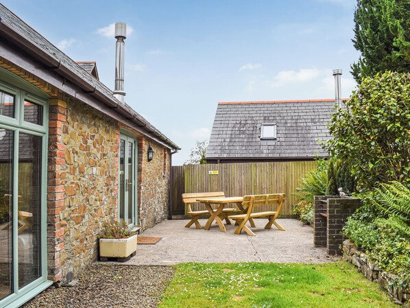 A stone building with a wooden deck, a table and chairs, and a small garden area.