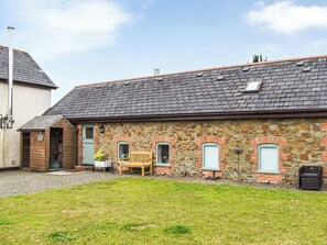 A stone building with a sloped roof, a wooden bench, and a small garden area.