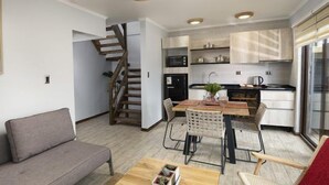 Una sala de estar moderna con un sofá, una mesa de comedor con sillas, una escalera y una zona de cocina con armarios y electrodomésticos.