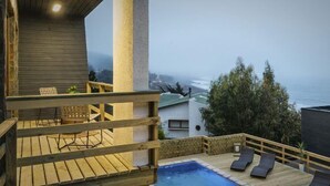 Una terraza de madera con piscina, sillas de descanso y vistas al océano.