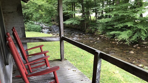A wooden porch with a railing overlooking a stream and forest. - Cabin 4 - Off the grid cabin at Pioneer Village (Maggie Valley)