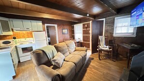 A cozy cabin interior with a wooden floor, a sofa, a dining table, and a kitchen area. - Cabin 4 - Off the grid cabin at Pioneer Village (Maggie Valley)