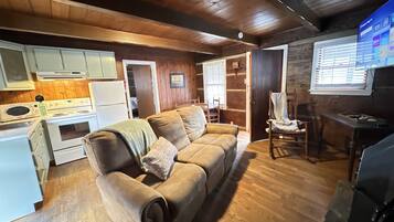 A cozy cabin interior with a wooden floor, a sofa, a dining table, and a kitchen area.