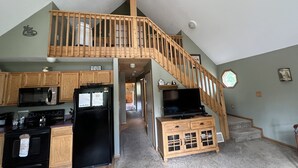 Une cuisine spacieuse avec des meubles en bois, un réfrigérateur noir et un escalier en bois menant à une mezzanine.