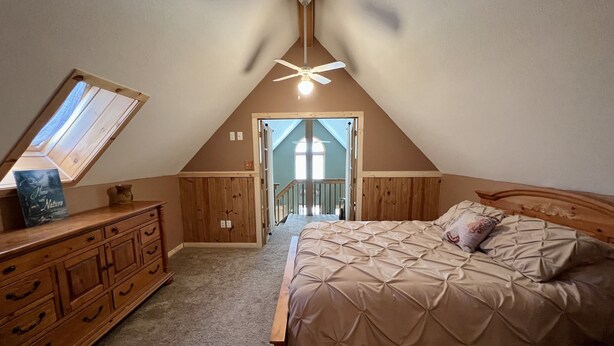 Une chambre avec un plafond en pente, un lit avec une tête de lit, une commode, une coiffeuse et un puits de lumière.