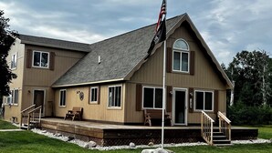 Une maison à deux étages avec un porche à l’avant, un mât pour drapeau et une petite terrasse.