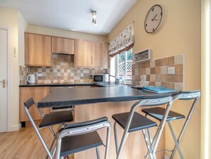 A compact kitchen with wooden cabinets, a microwave, a kettle, and a sink. There are four foldable chairs and a large window with a view.