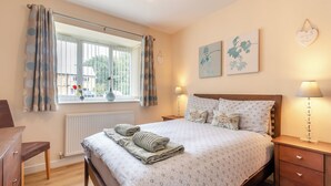A bedroom with a bed, bedside tables, a dresser, a window with curtains, and wall art. - 2 bedroom accommodation in Bridlington (Bridlington)
