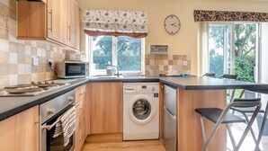A compact kitchen with a washing machine, a microwave, and a sink. - 2 bedroom accommodation in Bridlington (Bridlington)