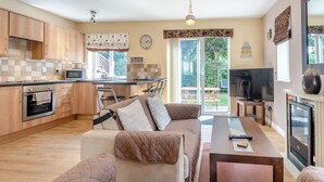 A modern kitchen with wooden cabinets, a microwave, and a built-in oven. There is a dining area with a sofa and a table, and a TV in the living room. - 2 bedroom accommodation in Bridlington (Bridlington)