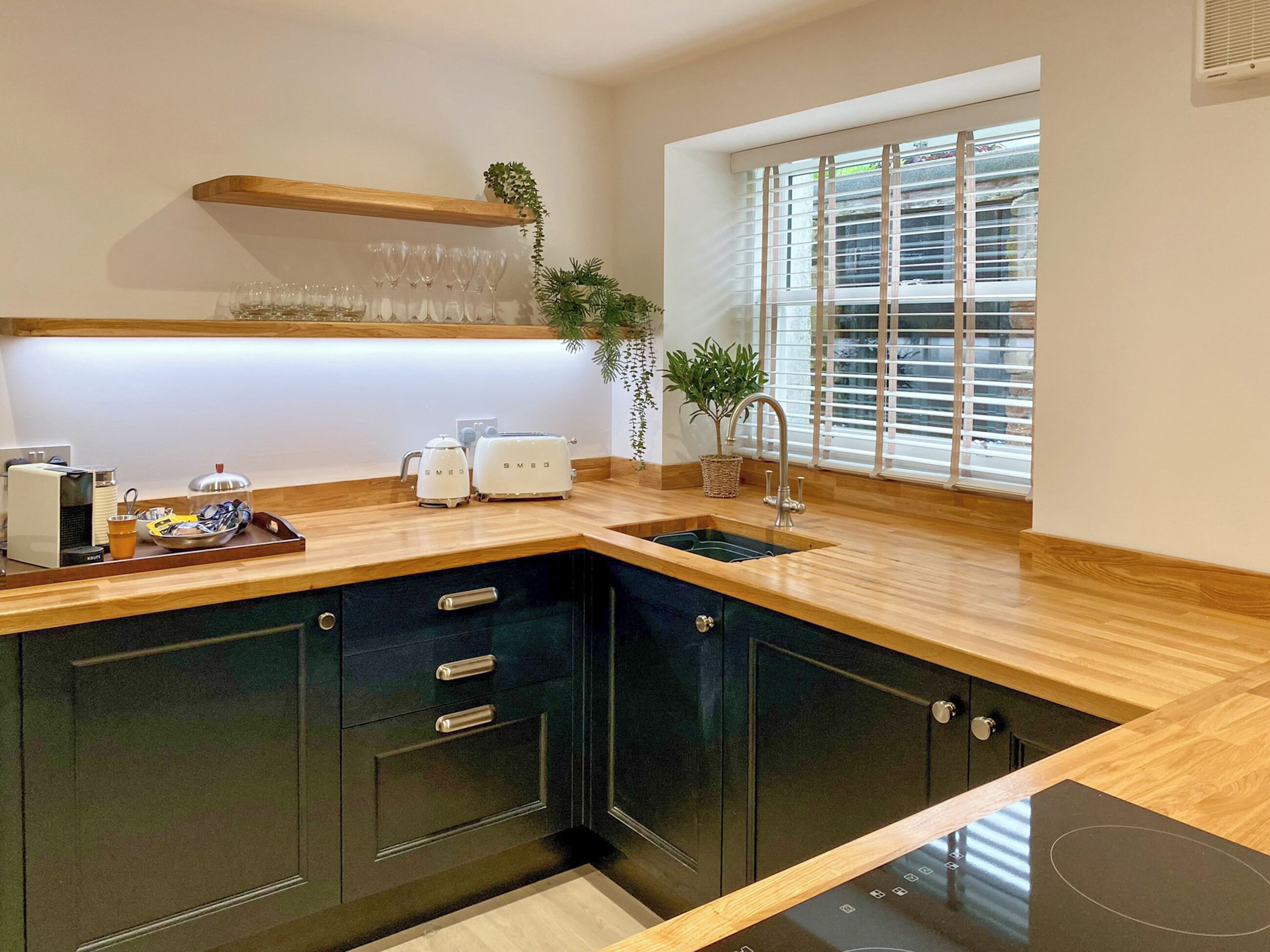 A modern kitchen with dark cabinets, a wooden countertop, a built-in sink, and a window with blinds.
