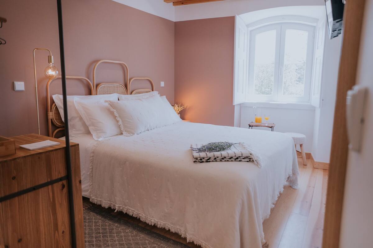 A bedroom with a bed, bedside table, lamp, and window.