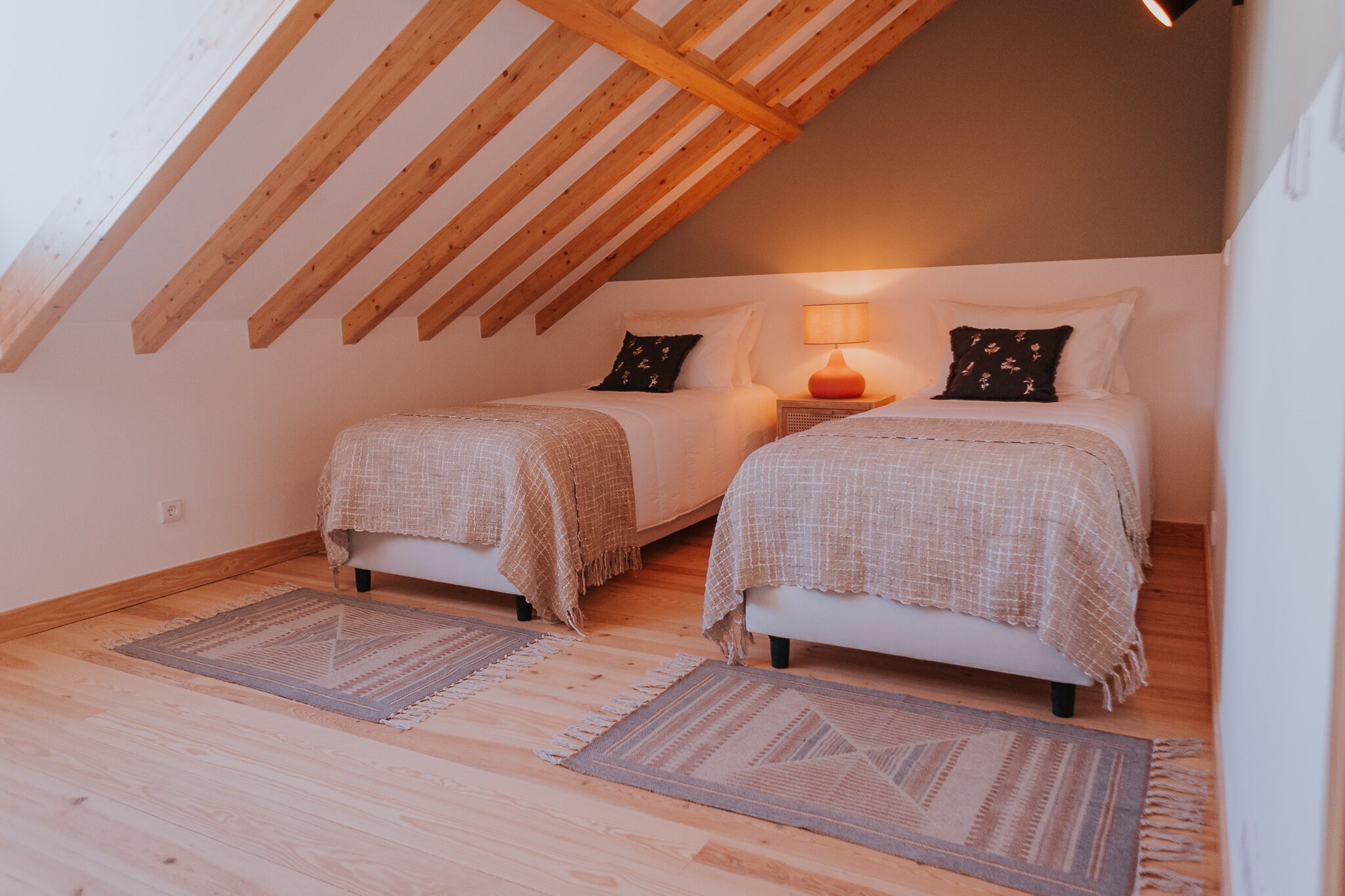 A cozy attic bedroom with two beds, wooden beams, and a lamp.