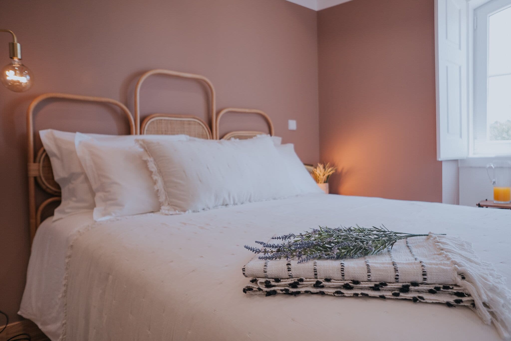 A neatly made bed with white linens, a headboard, and a bedside table with a lamp and a candle.