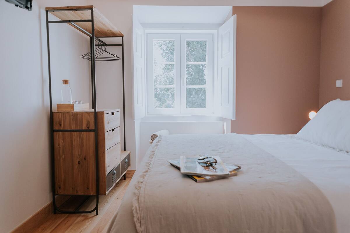 A bedroom with a bed, a wooden dresser, a window, and a white wall.