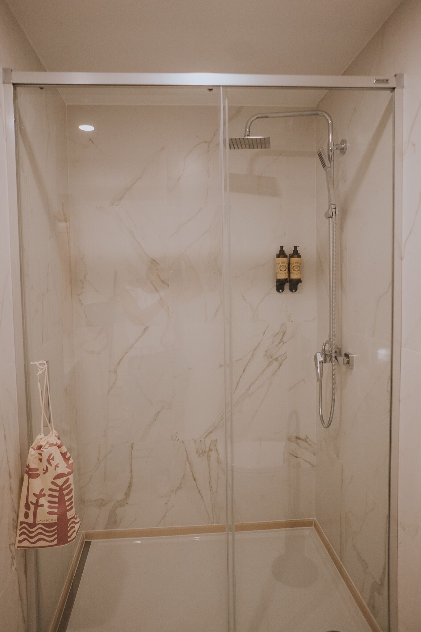 A glass-enclosed shower with a handheld showerhead and a wall-mounted faucet.